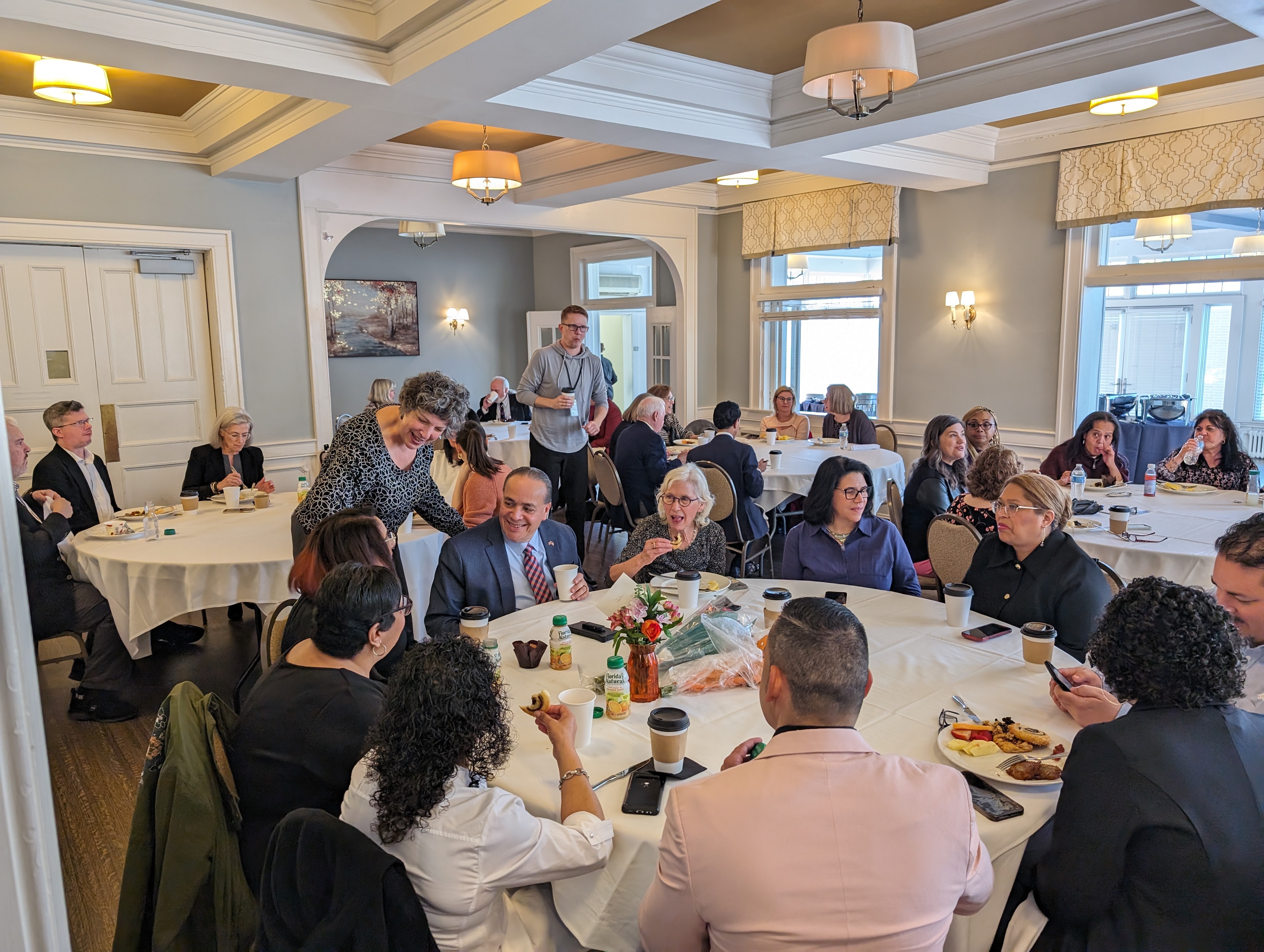 Many people sit around a circular table, chatting and engaged with each other.